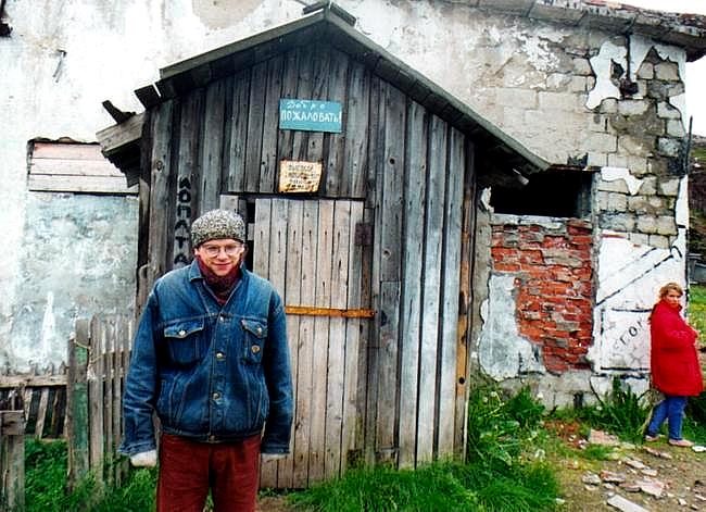Belarussian Yanek in front of a typical Teriberka dwelling. The blue sign above the door says, "Welcome."